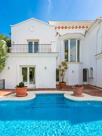 White villa façade with a first-floor balcony and a pool